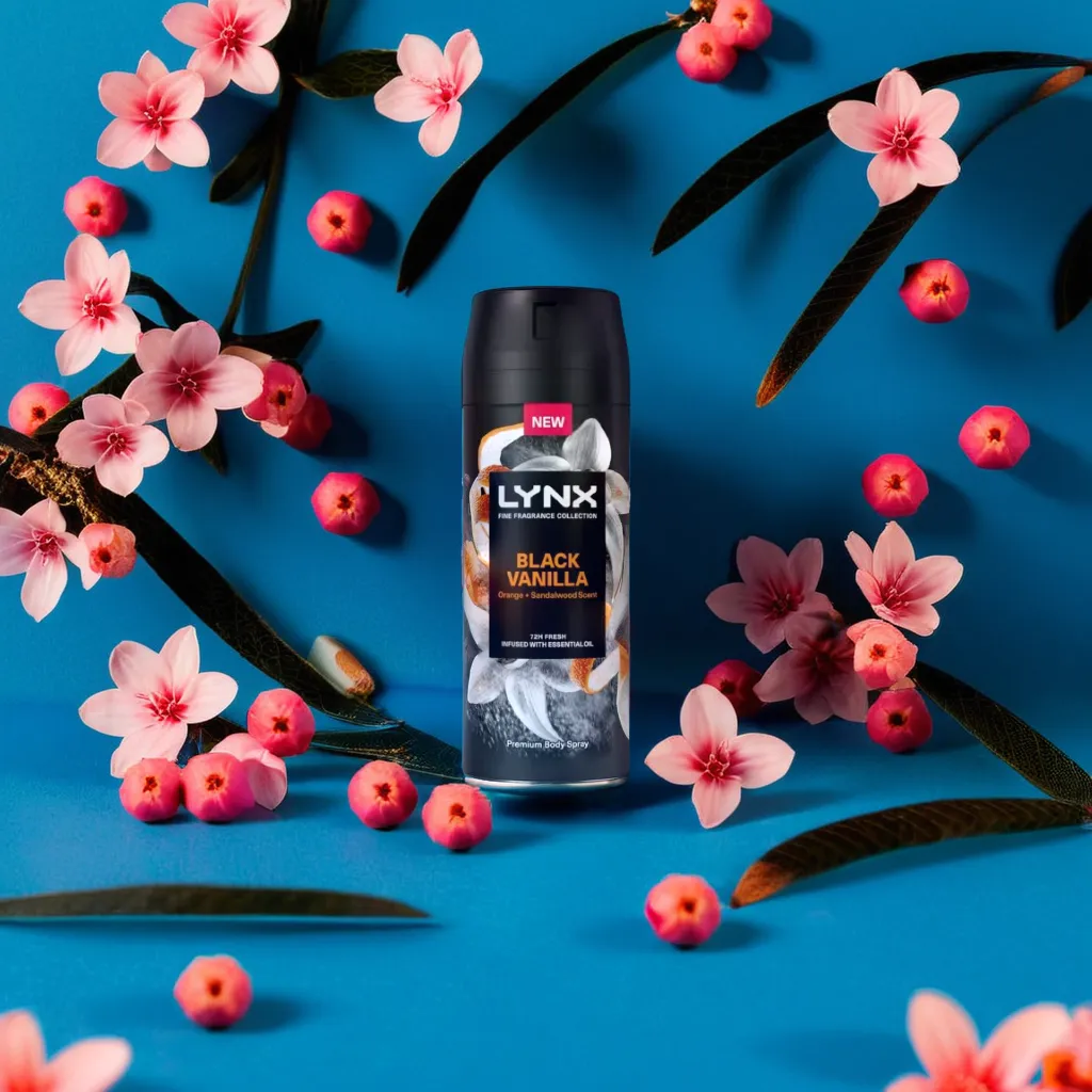 a can of body spray on a the ground of a blue room surrounded by little pink flowers and black vanilla